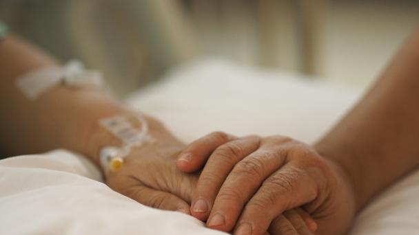Close up hands comforting patient in hospital bed.
