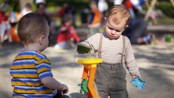 Two boys playing in a sand pit in a playground 