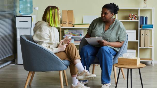 Two people sitting, talking - one young teen talking to older teacher or support worker.