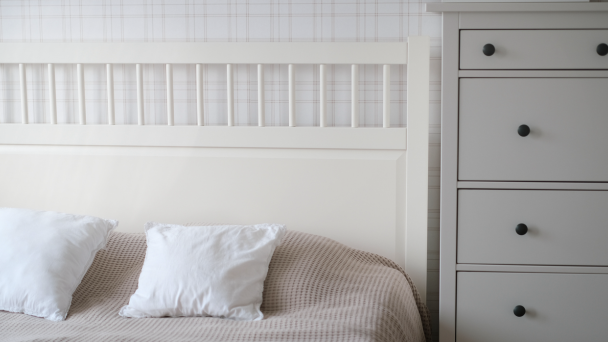Direct angle image of a bed and chest of draws next to it. 
