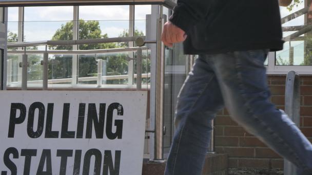 Polling station sign on the ground as someone unidentifiable walks by. 