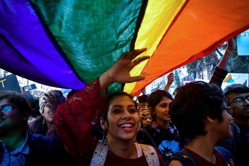 Image of a woman underneath a LGBTQ+ flag at a pride walk
