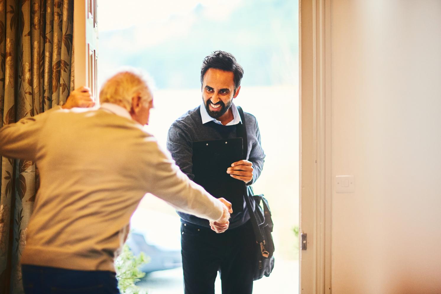 An older man opening the door to greet another man